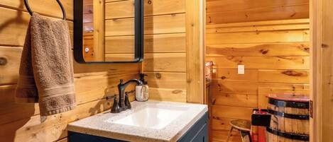 A wooden cabin bathroom with a sink, mirror, towel rack, and a barrel.