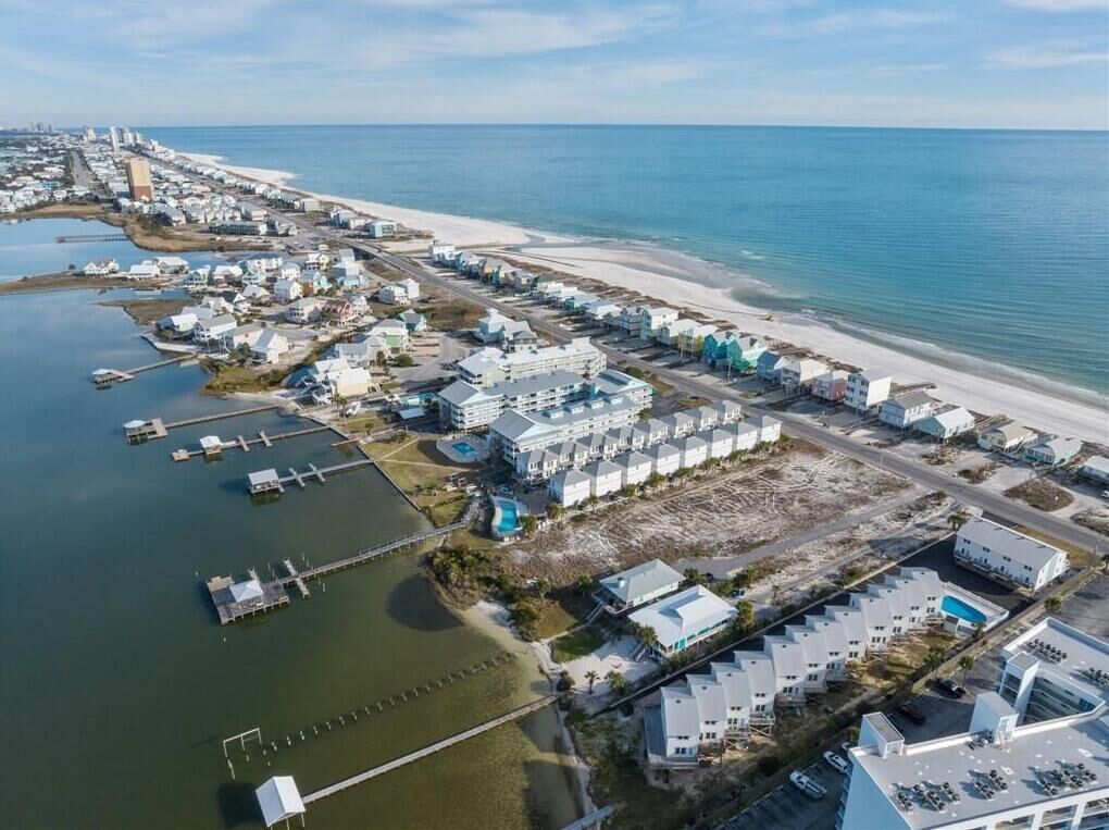 Luftaufnahme einer Küstenregion mit einem Yachthafen, Strand und mehreren Gebäuden, darunter ein großes Resort mit mehrstöckigen Bauten.