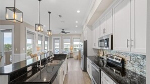 A modern kitchen with white cabinets, black countertops, and a large island. - Laguna Paradise (Gulf Shores)