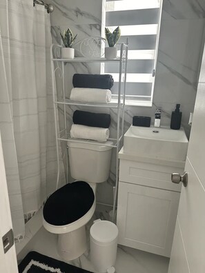 A compact bathroom with a toilet, a sink, and a shower area. - VillaClara Studio-Little Havana (Miami)