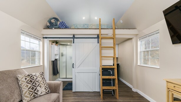 A loft bedroom with a bunk bed, a wooden ladder, a sliding door, and a view of the outdoors. - Two Tiny Homes, Close to Hiking & Hunting! (Pocatello)