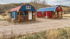Two small cabins with metal roofs and wooden decks, set in a dry, grassy area with hills in the background. - Two Tiny Homes, Close to Hiking & Hunting! (Pocatello)