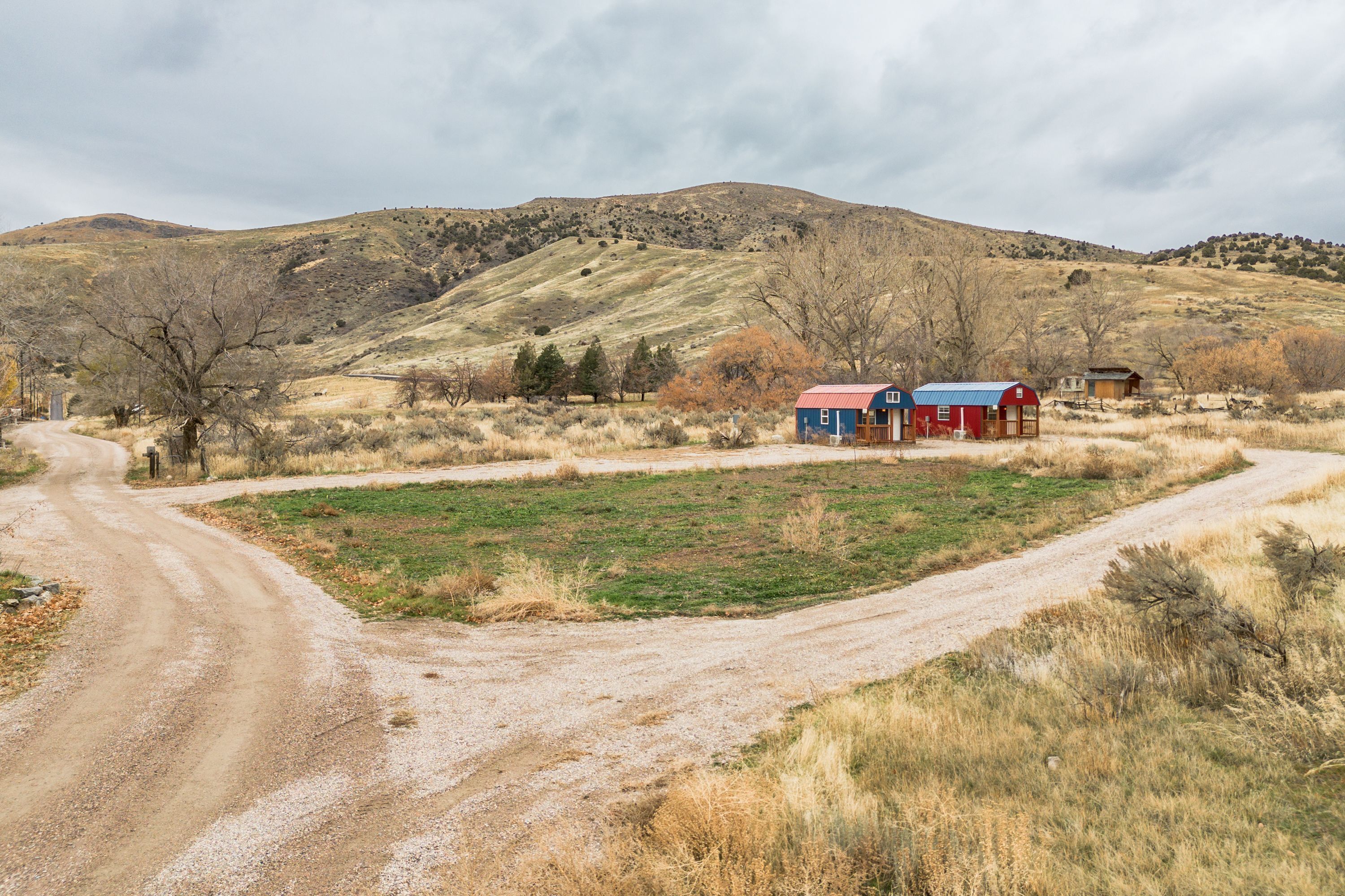 A rural landscape with a dirt road leading to a cluster of buildings with red roofs.