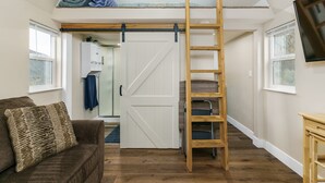 A loft bedroom with a wooden ladder, a sliding barn door, and a view of the outdoors. - Two Tiny Homes, Close to Hiking & Hunting! (Pocatello)