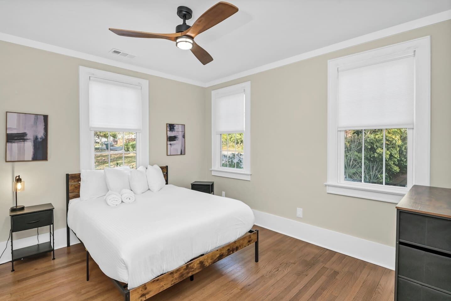 A bedroom with a bed, a ceiling fan, and two windows with blinds.
