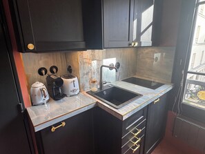 Eine kleine Küche mit dunklen Schränken, einer eingebauten Spüle, einem Toaster, einem Wasserkocher und einer Kaffeemaschine.
