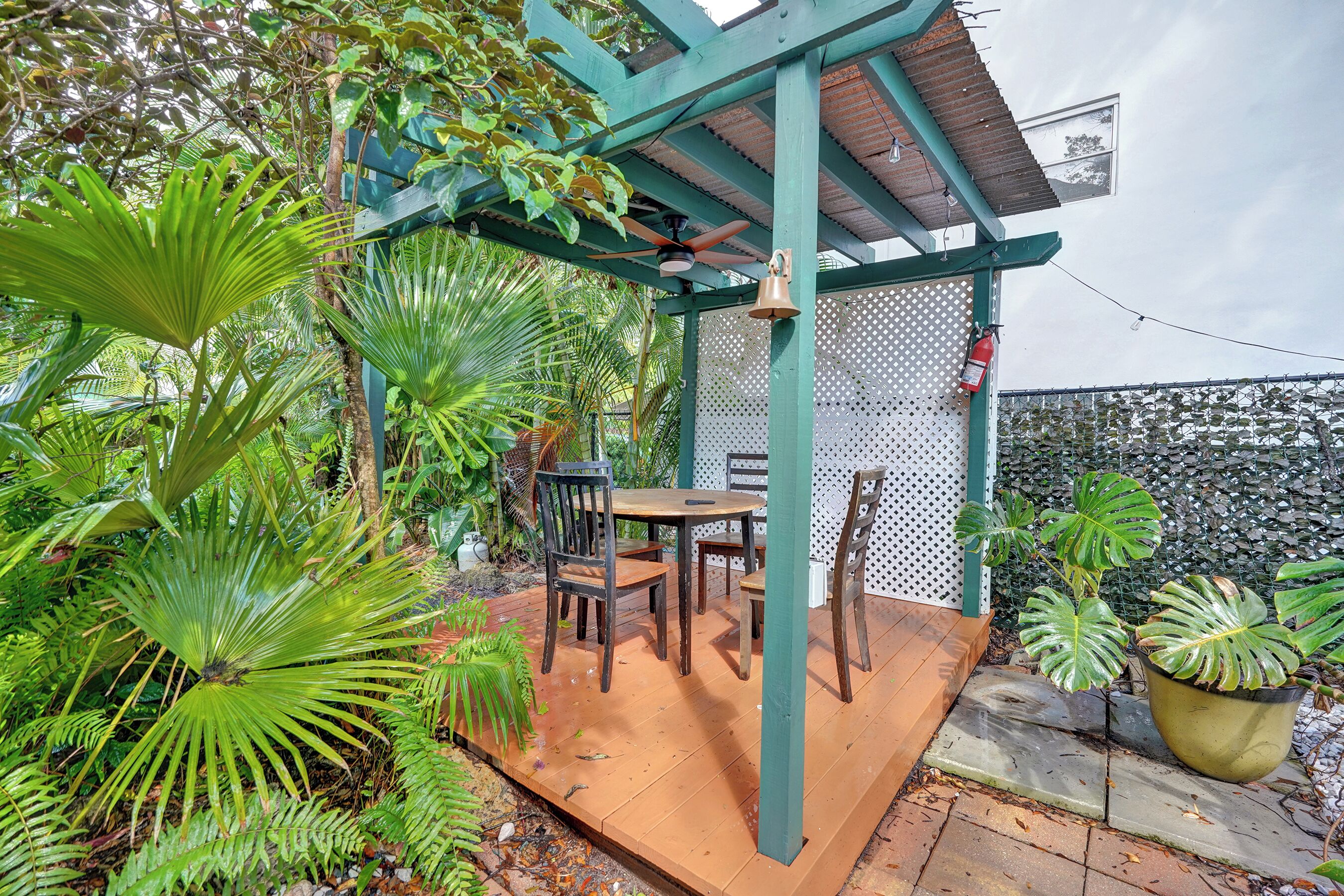 A covered patio area with a table and chairs, surrounded by lush tropical plants.