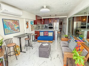 Ein modernes Wohnzimmer mit einem blauen Sofa, einem grauen Hocker und einem Essbereich mit einem Barhocker.