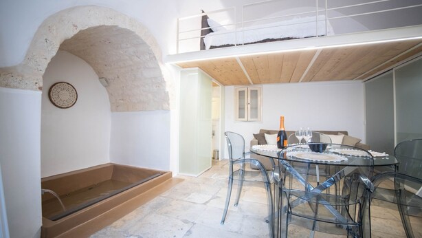 Un intérieur moderne avec une table à manger en verre, des chaises transparentes, une mezzanine en bois et une arche en pierre.