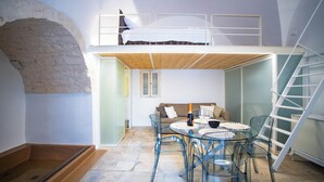 Une pièce de style loft avec un lit superposé, une table à manger en verre et un escalier.