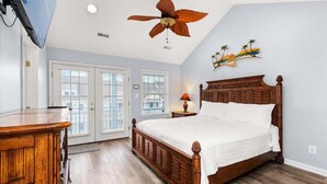 Una camera da letto con un letto in legno, una ventola a soffitto, un comodino con una lampada e un'opera d'arte appesa al muro.