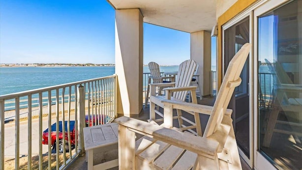 Een balkon met uitzicht op zee, met houten stoelen en een tafel.