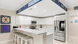 Een moderne keuken met witte kasten, een centraal eiland met barkrukken, roestvrijstalen apparatuur en decoratieve wandkunst.