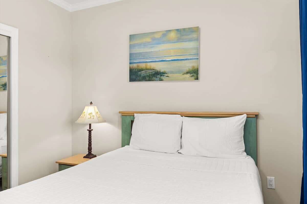A bedroom with a bed, a nightstand with a lamp, and a painting on the wall.