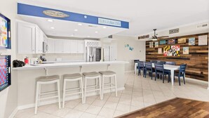 Een moderne keuken met witte kasten, een centraal eiland met krukken, en een eethoek met blauwe stoelen.