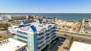 A multi-story hotel with a blue and white color scheme, located near a waterfront with a view of the sea. - The Bayside Oasis at Ocean Bliss | Boardwalk (Ocean City)