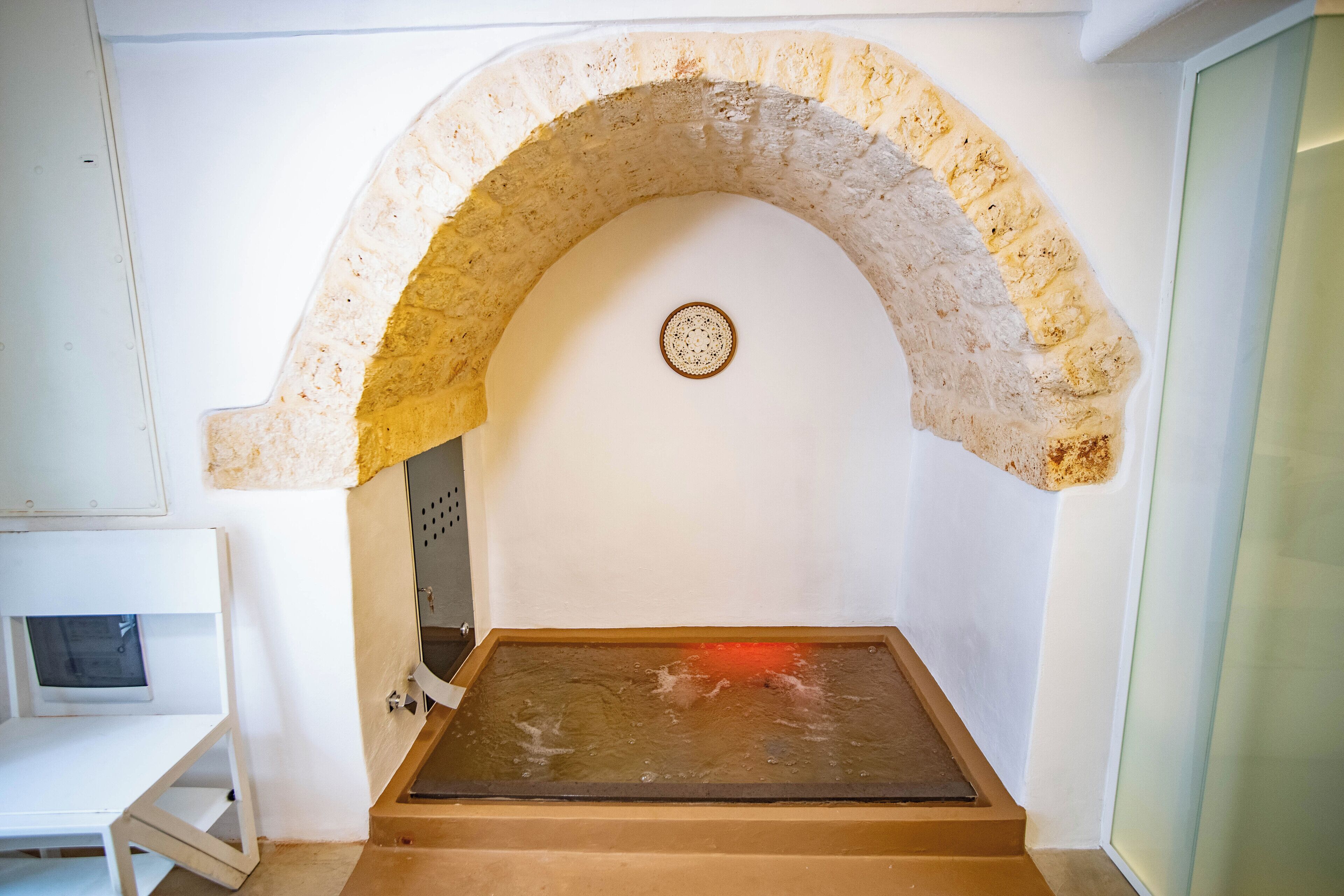 A room with a stone archway, a bed with a wooden headboard, and a small table.