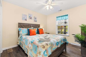 A bedroom with a bed, a ceiling fan, and a window with a view of greenery. - Coastal Tides & Pines | Dog Friendly (Ocean Pines)