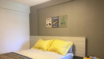 Quarto com cama, almofadas, mesa de cabeceira e três posters na parede.