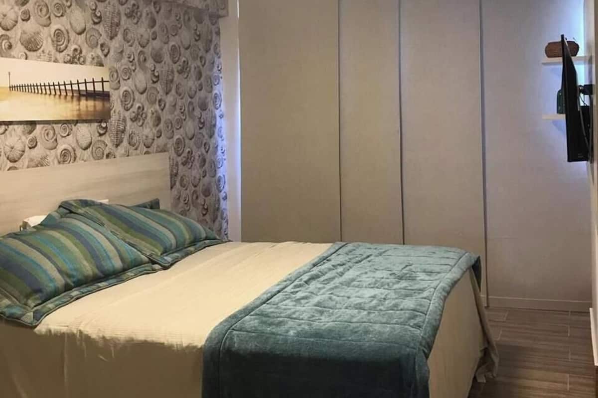 Un dormitorio con cama, cabecera, estante en la pared y armario.