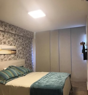 Un dormitorio con cama, cabecera, estante en la pared y armario.