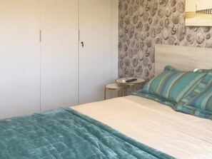 Een slaapkamer met een bed, nachtkastje, lamp en een kledingkast.