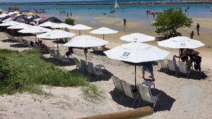A beach with rows of white umbrellas and lounge chairs, a sandy shore, and a clear blue sky. - La Fleur Polinésia Residence & Resort (Ipojuca)