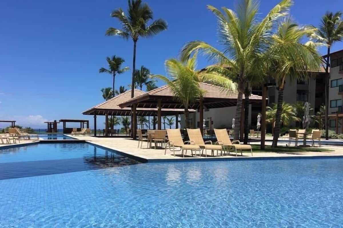 Una piscina con sillas de descanso y palmeras, rodeada de edificios.