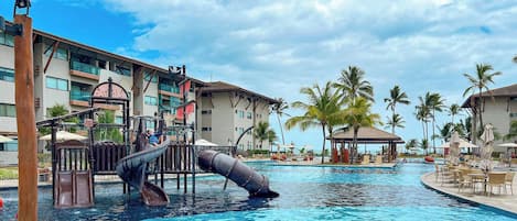 A swimming pool with a slide, palm trees, and a building with balconies.