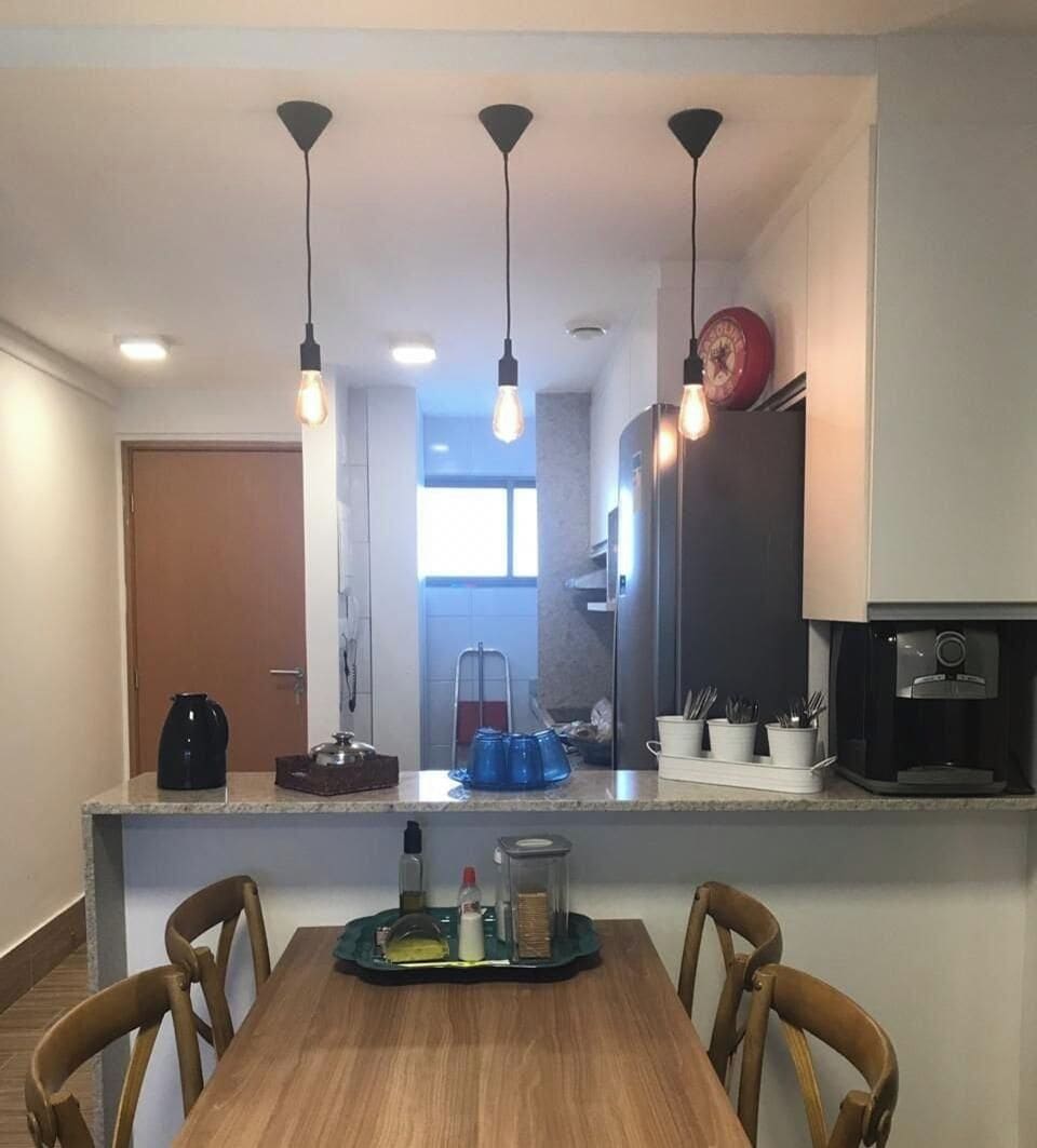 Cozinha compacta com ilha central, iluminação pendente e área de refeições com cadeiras.