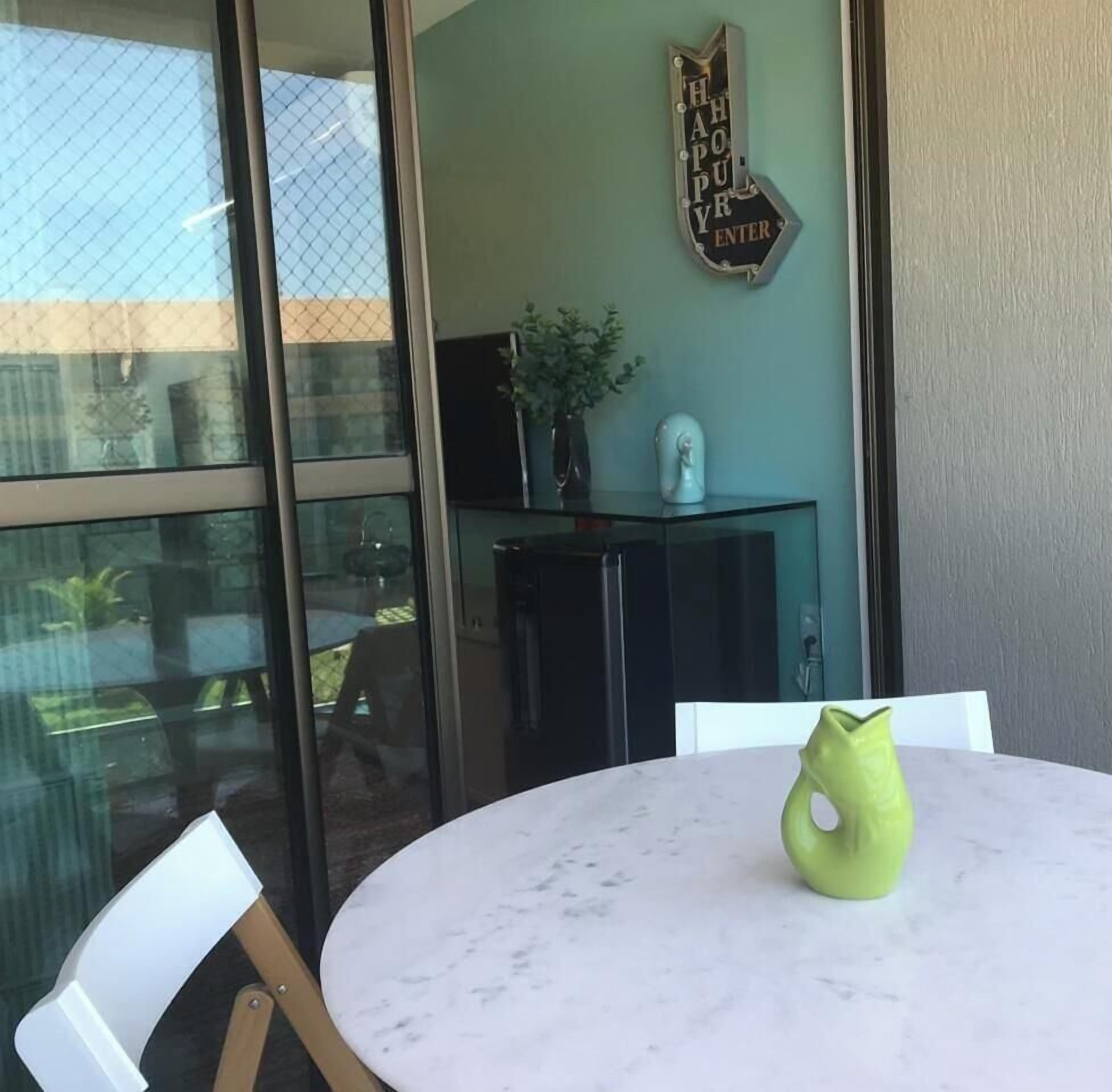 A room with a glass door, a round table with a green vase, a small plant, and a wall-mounted sign.