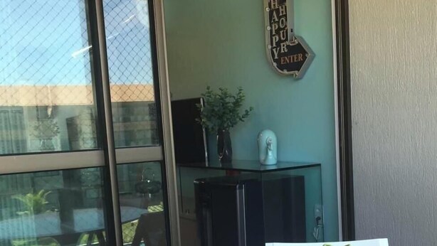 A room with a glass door, a round table with a green vase, a small plant, and a wall-mounted sign. - La Fleur Polinésia Residence & Resort (Ipojuca)