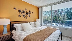 Un dormitorio con una cama grande, dos mesitas de noche, una decoración de pared con estrellas y vistas a árboles a través de un ventanal amplio.