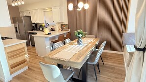 A modern kitchen with white cabinets, a central island, and a dining area with a wooden table and chairs. - Bright & Cozy 3-bedroom Family Stay with Arcade in Cedar Park (Cedar Park)