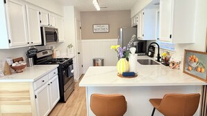 A modern kitchen with white cabinetry, a central island with two stools, a stove, and a sink. - Bright & Cozy 3-bedroom Family Stay with Arcade in Cedar Park (Cedar Park)