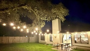 A backyard with a dining area, string lights, and a tree. - Bright & Cozy 3-bedroom Family Stay with Arcade in Cedar Park (Cedar Park)