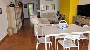 Un soggiorno con divano, tavolo da pranzo con sedie, televisore e una parete gialla.