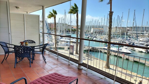 Un balcone con vista su un porto turistico, con un tavolo e sedie, e una ringhiera con palme.