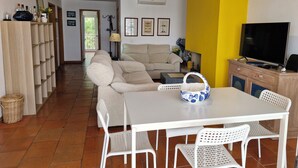 Un soggiorno con divano, tavolo da pranzo con sedie, televisore e libreria.