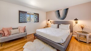 A modern bedroom with a large bed, a grey sofa, and a small side table. - Desert Oasis: Pool, Jacuzzi & 3BR Comfort (Yucca Valley)