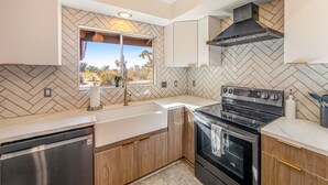 A modern kitchen with a herringbone tile backsplash, stainless steel appliances, and wooden cabinets. - Desert Oasis: Pool, Jacuzzi & 3BR Comfort (Yucca Valley)