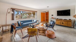 A modern living room with a blue sofa, leather chairs, a coffee table, and a flat-screen TV mounted on the wall. - Desert Oasis: Pool, Jacuzzi & 3BR Comfort (Yucca Valley)