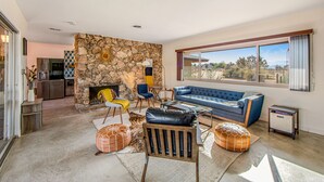 A modern living room with a stone wall, a blue sofa, and a view of the outdoors. - Desert Oasis: Pool, Jacuzzi & 3BR Comfort (Yucca Valley)