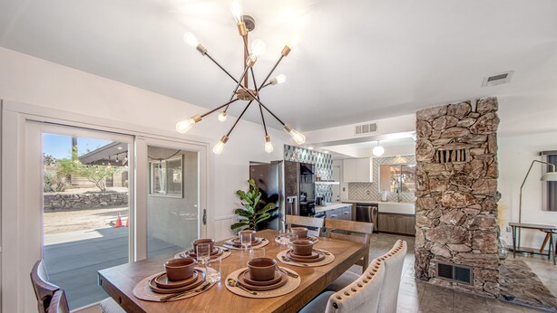 A dining area with a wooden table set for six, a stone accent wall, and a modern chandelier. - Desert Oasis: Pool, Jacuzzi & 3BR Comfort (Yucca Valley)