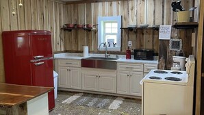 A kitchen with wooden paneling, a red refrigerator, a white stove, and a ceiling fan.