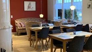 Een eetgedeelte met houten tafels en stoelen, een rode accentmuur en een groot raam met uitzicht op groen.