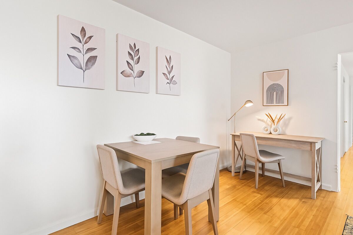 A dining area with a wooden table and chairs, a small plant on the table, and three leaf-patterned wall art pieces.