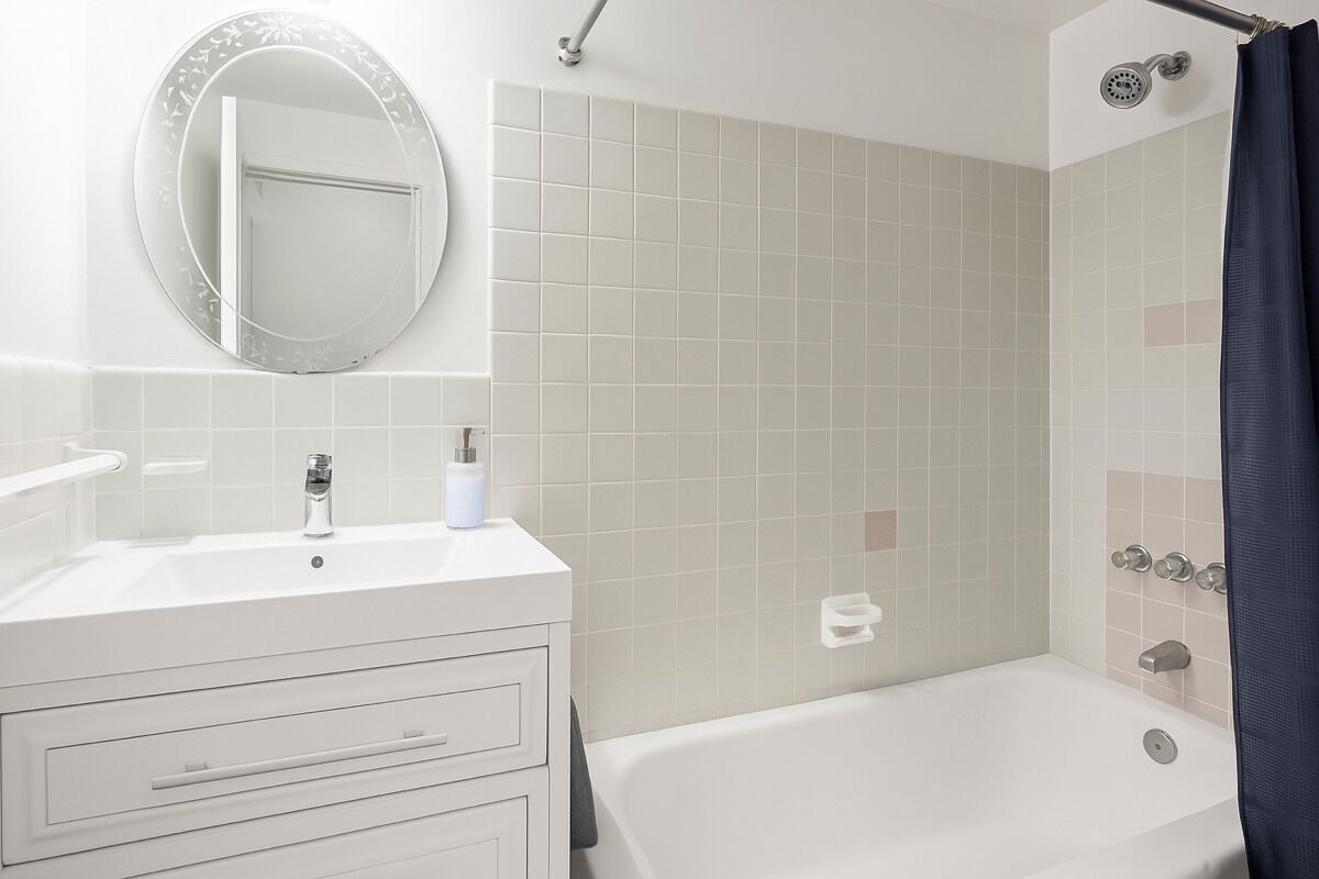 Un baño con tocador blanco, espejo redondo, bañera y zona de ducha con cortina.