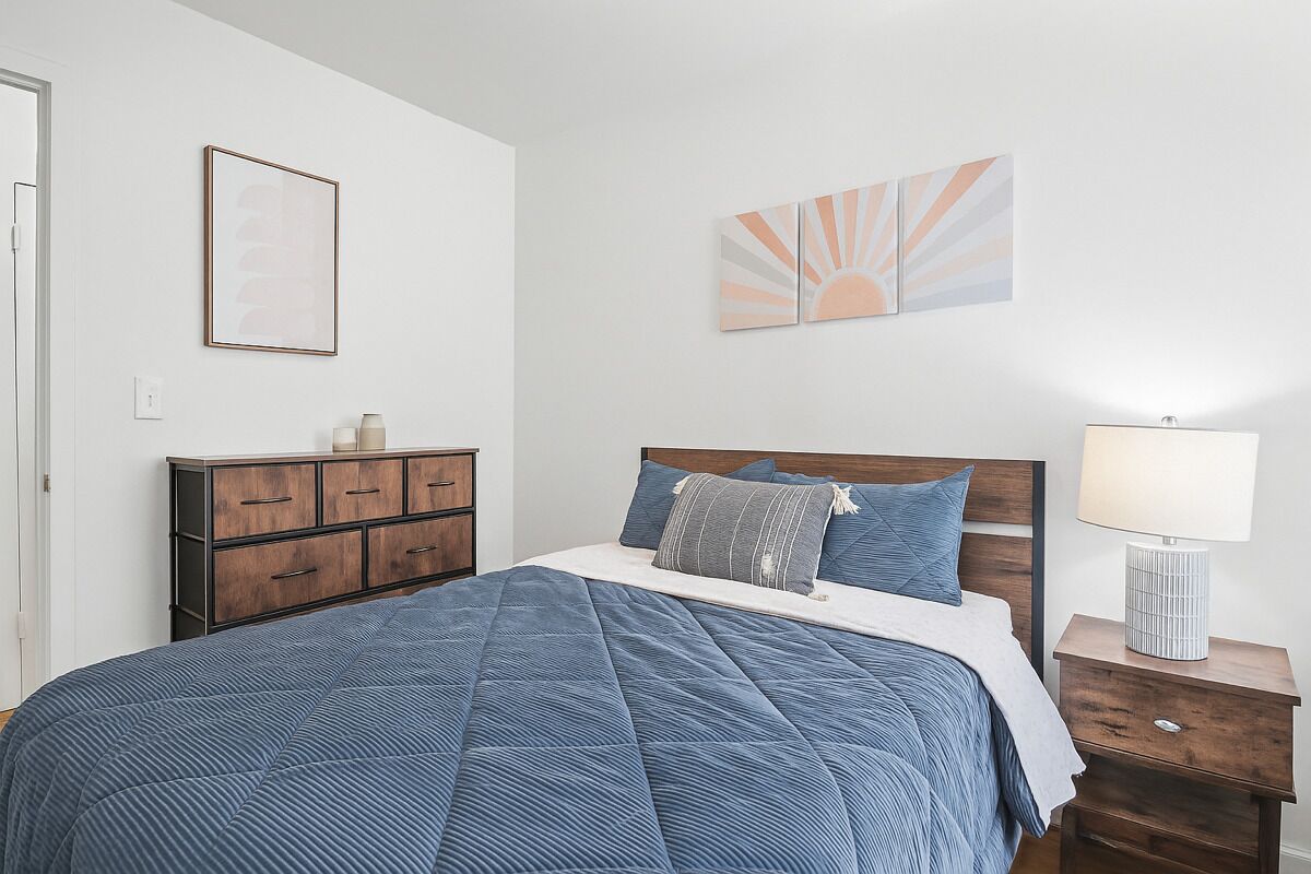 Ein Schlafzimmer mit einem großen Bett, einer Holzkommode, einem Nachttisch mit Lampe und zwei an der Wand befestigten Kunstwerken.