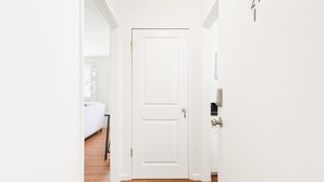 Ein Flur mit einer weißen Tür, Holzboden und einem weißen Sofa im Hintergrund.